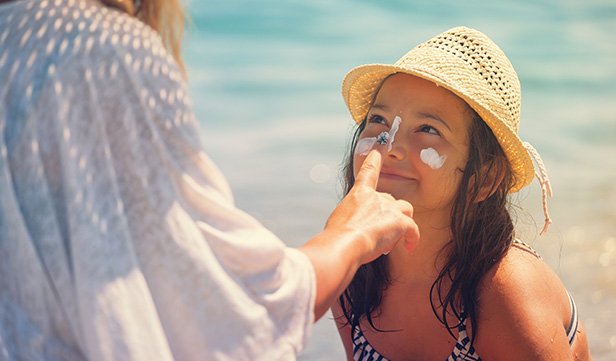 Mom applies sunscreen to young daughter’s face on day at the beach