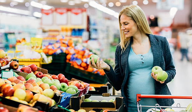 Pregnant woman with long hair shopping for produce in grocery store