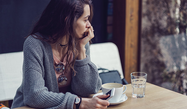 Woman sits alone in coffeeshop gazing out of a window