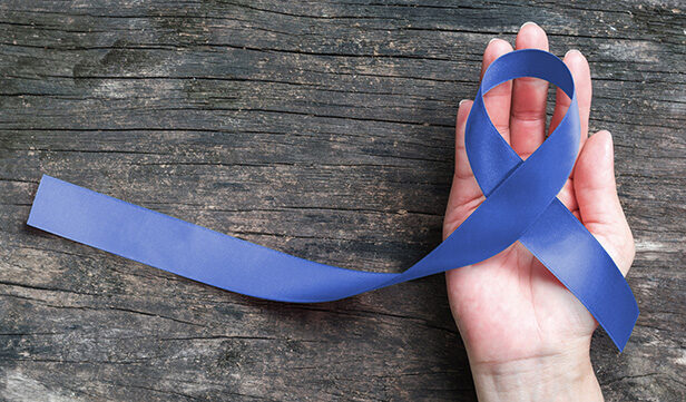 Open palm holds dark blue ribbon used to raise awareness of colorectal cancer