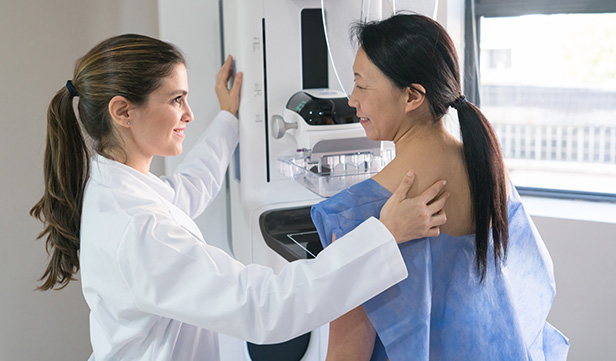 Mammogram technologist prepares woman in medical gown for breast cancer screening