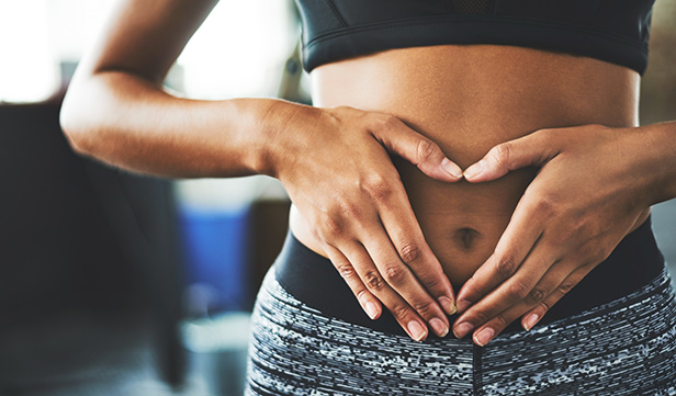 Woman in activewear holds her hands together in the shape of a heart over her stomach