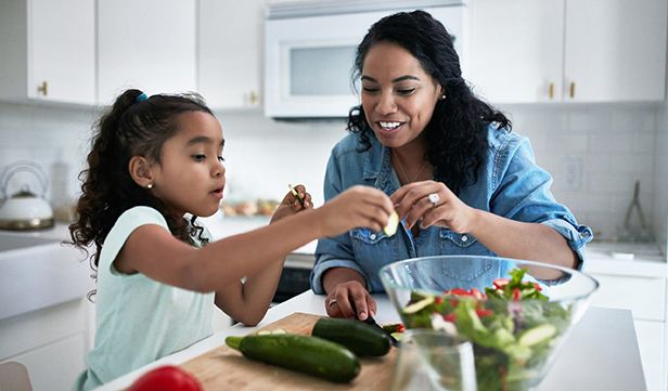 Mom wearing denim shirt and young daughter prepare a healthy salad in their kitchen