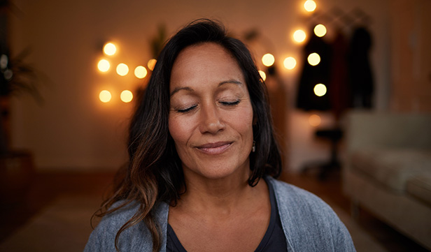 Serene woman with closed eyes practices relaxation techniques in her living room