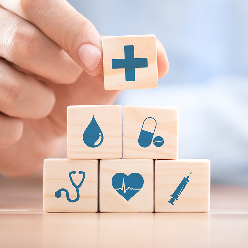 Six square wooden blocks with health-related icons are stacked into a pyramid