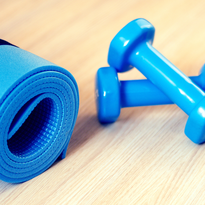 A pair of blue dumbbells sits on a hardwood floor beside a blue yoga mat